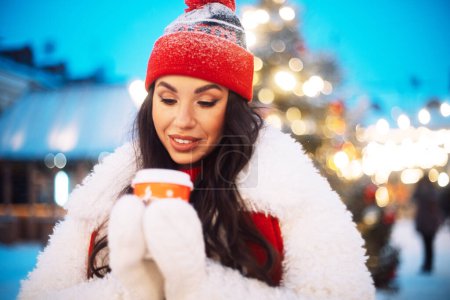 Photo for Beautiful happy young brunette woman in winter clothes at christmas market drinking coffee and smiling - Royalty Free Image