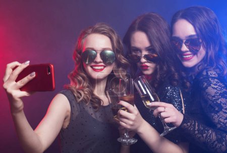 Photo for Group of partying young women clinking flutes with sparkling wine and holding disco balls and microphone, make selfie. Party time. - Royalty Free Image
