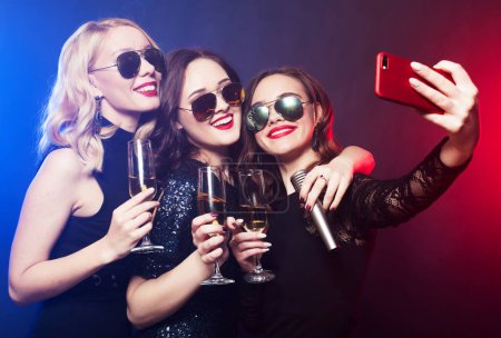 Téléchargez les photos : Group of partying young women clinking flutes with sparkling wine and holding disco balls and microphone, make selfie. Party time. - en image libre de droit