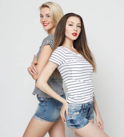Téléchargez les photos : Lifestyle, friendship and young people concept. Two cheerful and beautiful young women friends dressed in casual clothes posing together on a gray background. - en image libre de droit