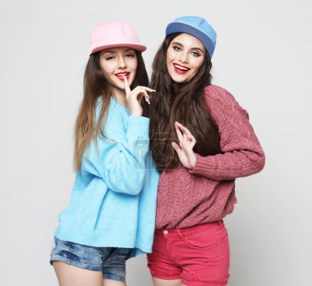 Foto de Two young female friends standing together and having fun over grey background - Imagen libre de derechos