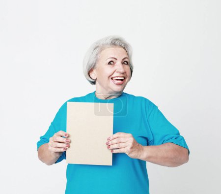 Téléchargez les photos : Mode de vie, émotion et concept de personnes âgées : Portrait de femme âgée heureuse portant un t-shirt bleu avec panneau publicitaire vierge ou un espace de copie sur fond blanc - en image libre de droit