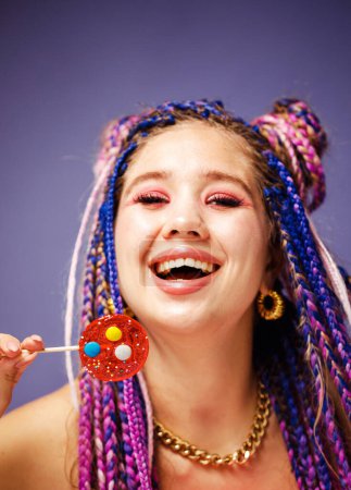 Foto de Mujer joven con peinado dreadlocks y maquillaje creativo en estilo muñeca con dulces sobre fondo púrpura. - Imagen libre de derechos