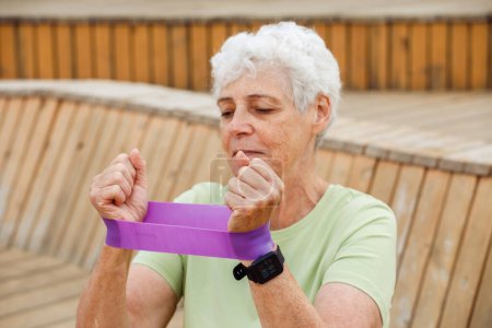 Téléchargez les photos : Portriat of elderly woman with grey short hair training with fitness band outdoow, summer day. Healthy lifestyle, old people and active retired life concept - en image libre de droit