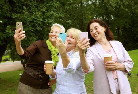 Photo for Three Caucasian pretty senior women friends smiling to smartphone camera while taking selfie photos. Old ladies posing to phone. Pensioners resting. - Royalty Free Image