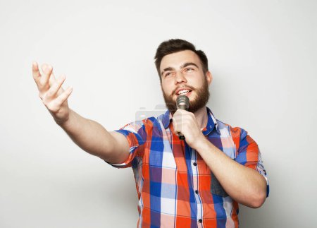 Foto de Estilo de vida, fiesta, emoción y concepto de personas. Un joven con barba sosteniendo un micrófono y cantando. De cerca.. - Imagen libre de derechos