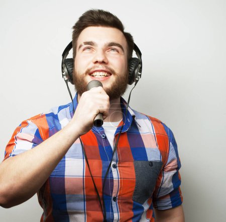 Foto de Concepto de estilo de vida: un joven con barba que lleva una camisa a cuadros que sostiene un micrófono y canta.. - Imagen libre de derechos
