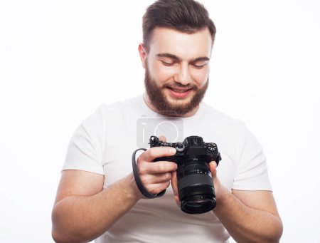 Téléchargez les photos : Mode de vie, tehnology et concept de voyage : homme barbu portant un t-shirt blanc avec un appareil photo numérique isolé sur un fond blanc - en image libre de droit