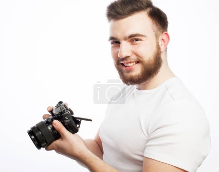 Foto de Estilo de vida, tehnología y concepto de viaje: hombre barbudo con camiseta blanca con una cámara digital aislada sobre un fondo blanco - Imagen libre de derechos