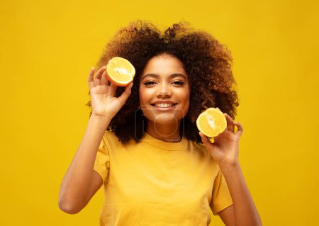 Téléchargez les photos : Style de vie, nourriture, régime alimentaire et concept de personnes : Photo de jeune femme afro-américaine tenir des tranches d'orange look étonné isolé sur fond de couleur jaune. - en image libre de droit