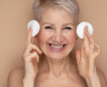 Photo for Medium Potrait: Beautiful Senior Woman Uses Cotton Wool Pad to Clean Her Perfect Face of Cosmetics. Smiling Elderly Lady with Soft Skin. Graceful Old Age and Natural Skincare Cleansing Product. - Royalty Free Image