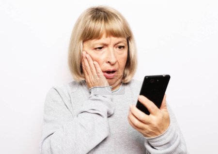 Téléchargez les photos : Une femme âgée lit de mauvaises nouvelles sur son smartphone et se sent malheureuse. Concept de style de vie et de personnes âgées. - en image libre de droit