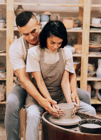 Téléchargez les photos : Couple in love working together on potter wheel in craft studio workshop. Lifestyle, people and hobby concept. - en image libre de droit