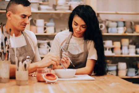 Foto de Una joven pareja encantadora trabaja en un taller de cerámica. Pintando un jarrón. El concepto de aficiones, estilo de vida y relaciones. - Imagen libre de derechos