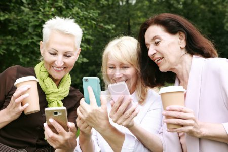 Photo for Charming old women laugh merrily and look at the screens of their smartphones. Having fun in retirement on a summer afternoon. Golden age. - Royalty Free Image