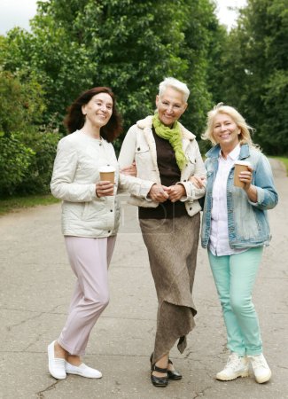 Téléchargez les photos : Lifestyle, friendship, old people and gold age concept. Three elderly ladies in casual clothes are walking in the park. Coffee and socializing, friendship in retirement. - en image libre de droit