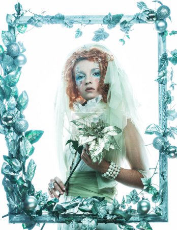 Foto de Party, christmas and people concept: A beautiful ginger woman in a costume for the Christmas carnival poses in a frame of Christmas decorations and holding a flower. Winter style, snow queen. - Imagen libre de derechos