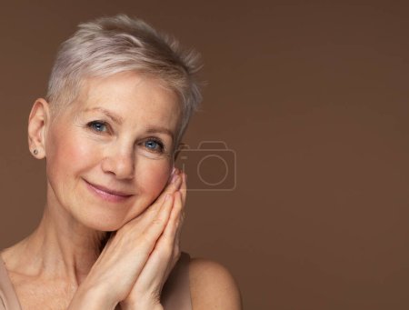 Téléchargez les photos : Portrait de beauté de femme mûre souriant avec la main sur le visage. Visage rapproché d'une femme âgée heureuse se sentant fraîche après un traitement anti-âge. Beauté souriante regardant la caméra avec une peau parfaite. - en image libre de droit