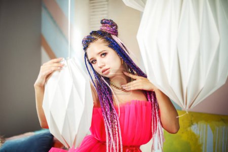 Photo for Caucasian young pretty woman with dreadlocks hairstyle wearing pink dress, doll style, bright make, up in the pink room. - Royalty Free Image
