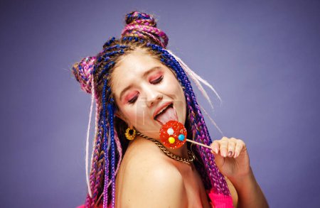 Foto de Mujer joven con peinado dreadlocks y maquillaje creativo en estilo muñeca con dulces sobre fondo púrpura. - Imagen libre de derechos