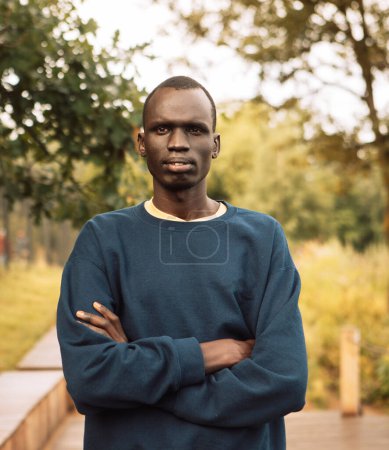 Foto de Retrato de un joven africano que está de pie con los brazos cruzados en un día de verano en el parque, estilo de vida - Imagen libre de derechos