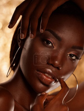 Foto de Mujer joven hermosa de piel oscura posando sensualmente sobre un fondo dorado. Piel impecable con maquillaje brillante. - Imagen libre de derechos