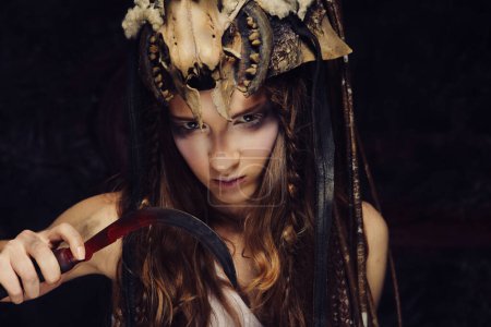 Foto de Mujer joven con maquillaje agresivo sosteniendo una hoz. Halloween. Fiesta de disfraces. - Imagen libre de derechos
