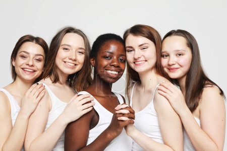 Foto de Portrait of young charming multiracial female friends over light grey background. Lifestyle, friendship and people concept. - Imagen libre de derechos