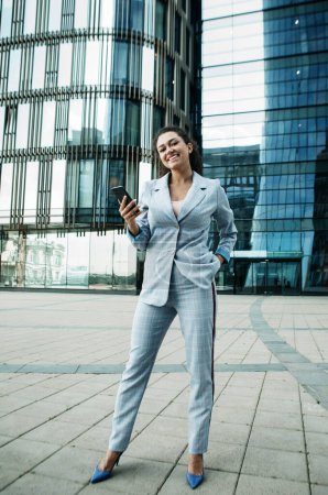 Foto de Young mulatto business woman uses a mobile phone in front of a modern business center - Imagen libre de derechos