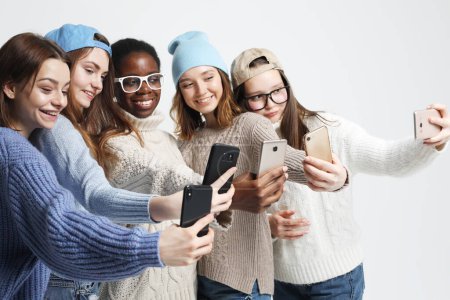 Foto de Diverse multi nation female group, african-american and caucasian teenage friends company make selfie with smartphones over grey background - Imagen libre de derechos