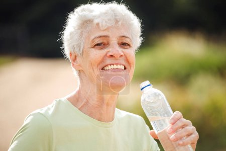 Foto de Senior woman with short grey hair drinking water after exercising, summer time, portrait in the park - Imagen libre de derechos
