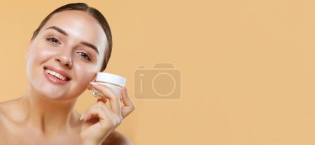 Photo for Concept of using moisturizing cream before going to bed. Beautiful cute pretty charming woman is holding a cream jar isolated on beige background - Royalty Free Image