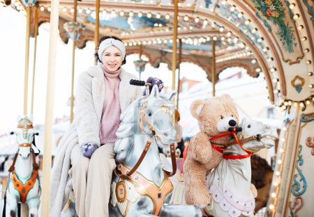 Photo for Pretty woman saddled a horse on a carousel. Christmas market, happiness and fun. - Royalty Free Image