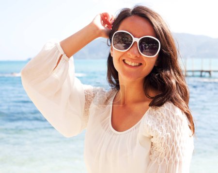 Téléchargez les photos : Femme heureuse en robe blanche d'été et lunettes de soleil sur la plage. Femme caucasienne relaxant et profiter de la paix en vacances. - en image libre de droit