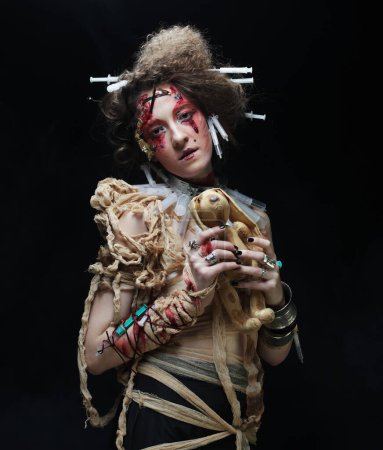 Foto de Mujer joven en estilo zombi sosteniendo un conejito de juguete en sus manos, sobre un fondo oscuro. Maquillaje brillante y peinado. Concepto del partido. - Imagen libre de derechos
