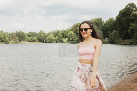 Téléchargez les photos : Une belle jeune femme en vêtements décontractés se promène le long de la plage près du lac. Bon été. - en image libre de droit