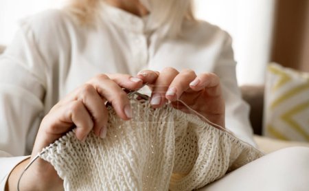 Téléchargez les photos : Les mains de la femme tricot motif de fil de laine blanche. Photo horizontale rapprochée. Freelance concept d'artisanat créatif, passe-temps et mode de vie - en image libre de droit