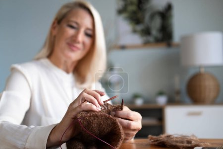 Photo for For my children. Happy delighted aged woman holding knitting needles and smiling while making a scarf. Lifestyle and people concept. - Royalty Free Image