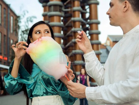 Photo for Beautiful young smiling couple walking down the street eating cotton candy and having great summer time. Love, date,romance, lifestyle concept. - Royalty Free Image