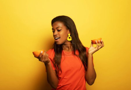 Téléchargez les photos : Été sain, régime alimentaire et concept de personnes : Joyeux jeune femme africaine tenant des oranges sur fond jaune - en image libre de droit