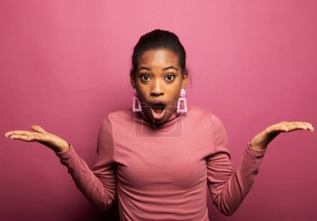 Foto de Retrato de una joven mujer negra sintiéndose emocionada, gritando OMG o WOW, expresando emoción de alegría en el fondo rosa del estudio. - Imagen libre de derechos