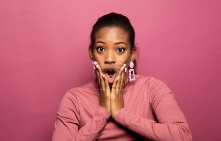 Photo for Surprised beautiful black woman holds cheeks by hand over pink color background. People, reaction, ethnicity concept, - Royalty Free Image