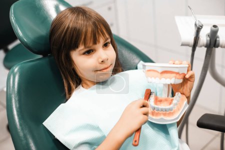 Photo for Child girl after the doctor at the clinic, holding a dental jaw and brush teeth in her hands. People, medicine, stomatology, technology and health care concept. - Royalty Free Image