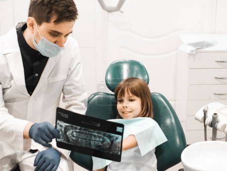 Téléchargez les photos : Les gens, la médecine, la stomatologie, la technologie et le concept de soins de santé - dentiste masculin montrant des radiographies des dents à une enfant fille au cabinet de la clinique dentaire. - en image libre de droit