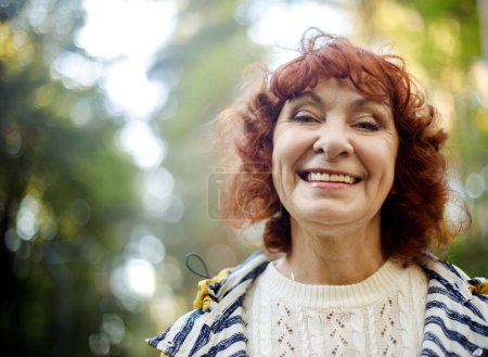 Foto de Retrato de una feliz anciana riendo con el pelo rizado rojo en el parque. Día de otoño. - Imagen libre de derechos