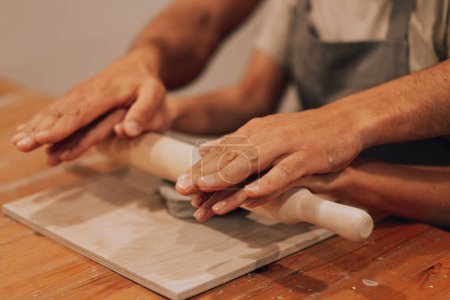 Foto de Las manos masculinas y femeninas trabajan en un taller de cerámica. Despliegue la cerámica con un rodillo. Estilo de vida. - Imagen libre de derechos