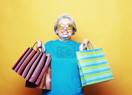 Téléchargez les photos : Lifestyle, shopping and old people concept: Happy mature woman with shopping bags isolated on yellow background - en image libre de droit
