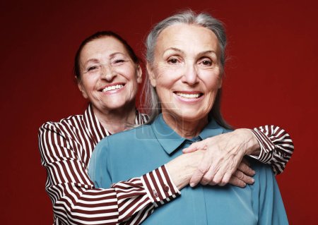 Téléchargez les photos : Lifestyle, love, friendship and old people concept. Two elderly women friends hugging on red background. - en image libre de droit