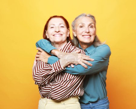 Téléchargez les photos : Lifestyle, love, friendship and old people concept. Two elderly women friends hugging on yellow background. - en image libre de droit