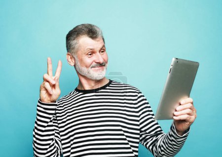 Photo for Lifestyle, tehnology and old people concept. Charming elderly man communicates with friends using a digital tablet over blue background. - Royalty Free Image